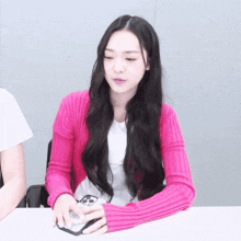 a woman wearing a pink sweater is holding a cell phone