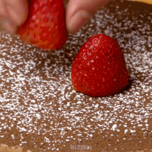 a strawberry on top of a chocolate cake with powdered sugar on it