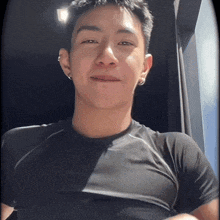 a young man wearing a black shirt and earrings smiles for the camera