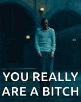 a man in a white sweater is standing in front of a building with the words `` you really are a bitch '' .