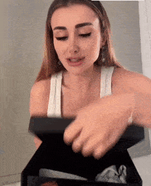 a woman in a white tank top opens a box