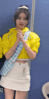 a girl wearing a yellow jacket and a white skirt is standing in front of a blue wall