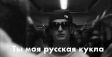 a black and white photo of a man wearing sunglasses and a hat with russian writing on it .