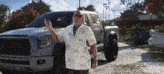 a man in a hawaiian shirt stands in front of a silver truck