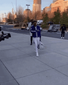 a man in a blue jacket and white pants walking down a sidewalk