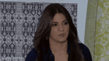 a woman in a blue shirt stands in front of a wall that has a pattern on it and the words sitemaperrobi on the bottom