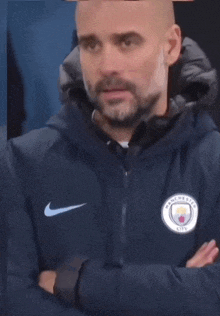 a man with a beard wearing a nike jacket with manchester city written on it