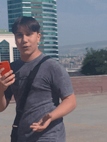 a young man in a gray shirt is holding a red cell phone