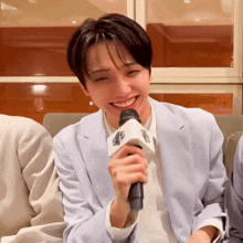 a young man in a suit is smiling while holding a microphone that says smfc