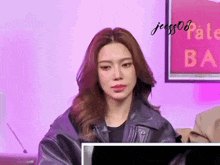 a woman in a black leather jacket is sitting in front of a computer monitor .