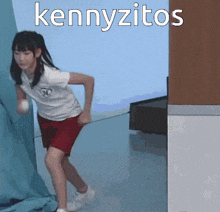 a girl in a white shirt and red shorts is running in front of a sign that says kennyzito 's