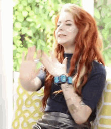 a woman with red hair and a watch on her wrist is sitting in a chair with her eyes closed .