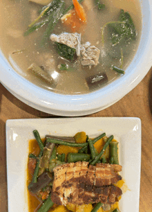 a bowl of soup next to a plate of vegetables and meat