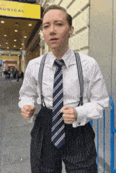 a man wearing suspenders and a tie is standing in front of a building that says musical