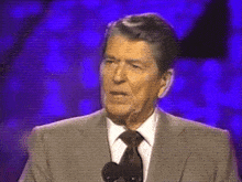 a man in a suit and tie stands in front of a microphone
