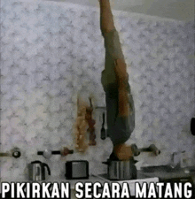 a man is doing a handstand in a kitchen with a pot on top of his head .