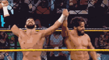 two men in a wrestling ring with their arms in the air and a crowd in the background