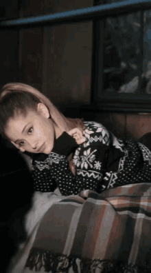 a woman laying on a bed wearing a black sweater with snowflakes on it