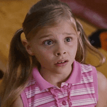 a little girl in a pink and white striped shirt looks surprised