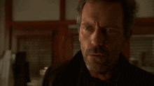 a man with a beard and a black jacket looks at the camera