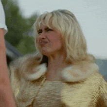 a woman with blonde hair is wearing a gold jacket and making a funny face .