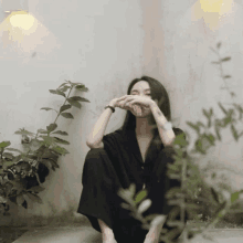 a woman covering her face with her hands while sitting in front of a plant