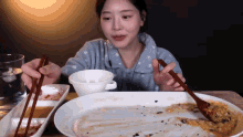 a woman is sitting at a table with chopsticks and a plate of food