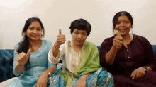 three women are sitting on a couch and giving thumbs up