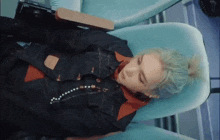 a man with green hair is laying in a chair with his eyes closed .