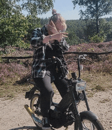 a woman in a plaid shirt is sitting on a motorcycle on a dirt road
