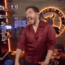 a man in a red shirt is dancing in front of a sign that says son of ram shop
