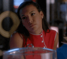 a woman in a red top with white buttons looks at the camera