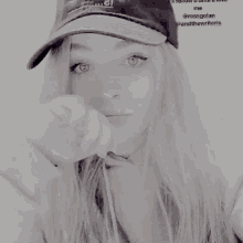 a woman wearing a hat and a white sweater is covering her face with her hand .