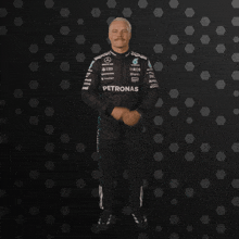 a man wearing a petronas jumpsuit is standing in front of a black background