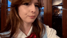 a woman wearing a white shirt and a red bow tie looks at the camera