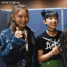two girls are standing next to each other and one is giving a thumbs up sign .