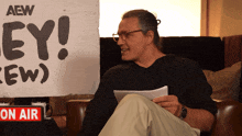 a man is sitting in front of a sign that says aew