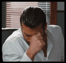 a man in a white shirt is rubbing his forehead