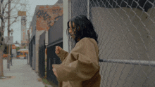 a woman leaning against a chain link fence with graffiti on the wall behind her that says motel