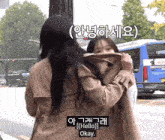 a woman in a trench coat is hugging another woman and says hello okay