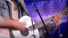 a man is playing a guitar in front of a microphone with the nbc logo in the background