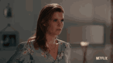 a woman in a floral shirt is looking up with a netflix logo in the background