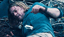 a man in a blue shirt is laying on the ground in a pile of wires