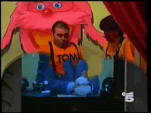 a man wearing a shirt that says tom stands in front of a red monster