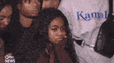 a woman wearing a kamal shirt is sitting in a crowd of people