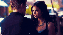 a man and a woman are standing next to each other and the woman is wearing a necklace