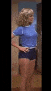 a woman in shorts and a blue shirt is standing in a doorway .