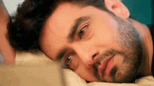 a man with a beard is laying on a bed with his head on a pillow and looking at the camera .