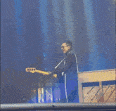 a man is playing a bass guitar and singing into a microphone on stage .