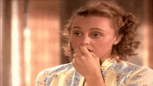 a woman covering her mouth with her hand and wearing a floral shirt